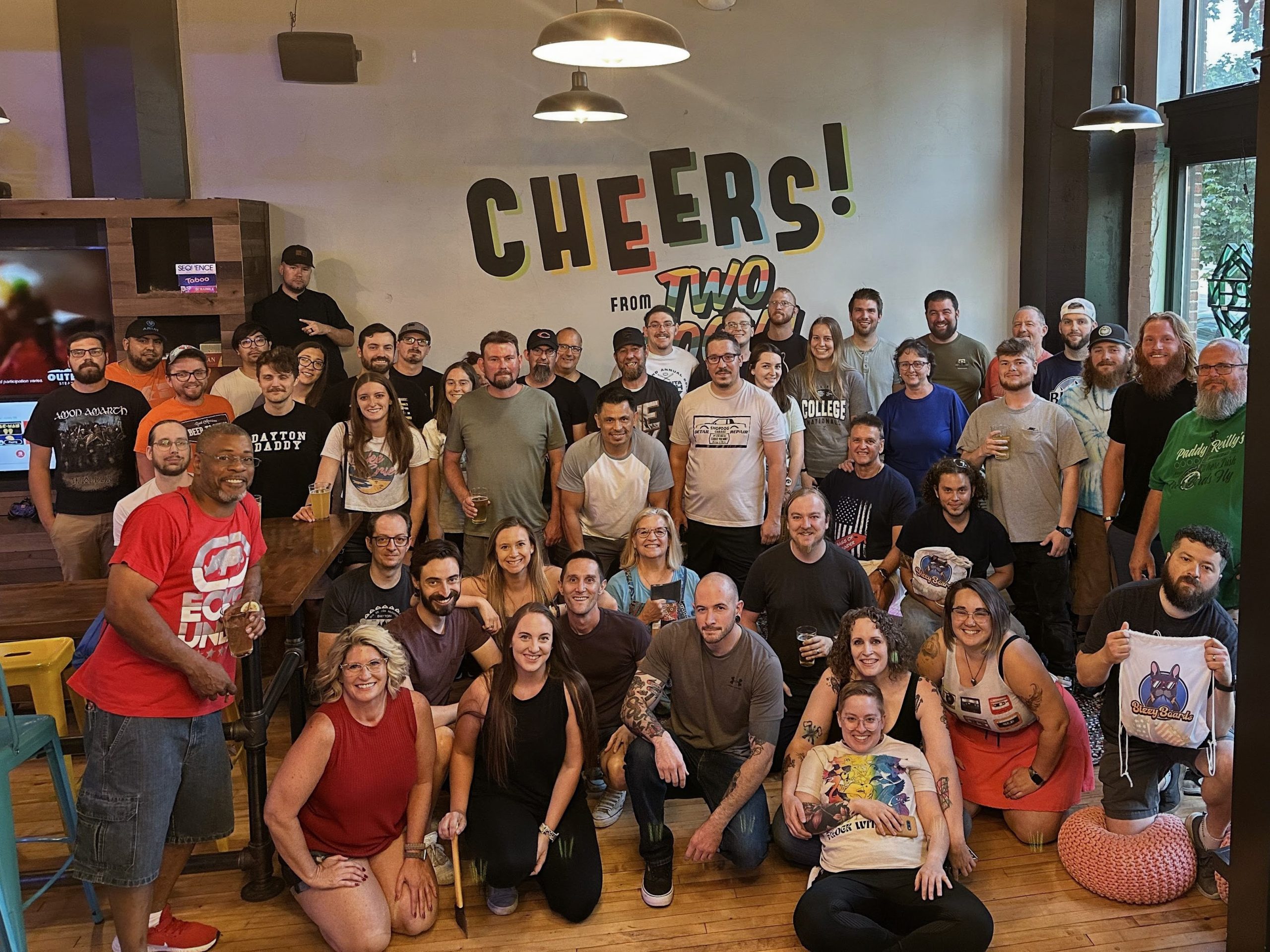 Large group of smiling adults gathered inside Two Social in Dayton, Ohio, posing for a group photo under a colorful “Cheers from Two Social” mural, celebrating Gem City Social Sports’ community and league events.